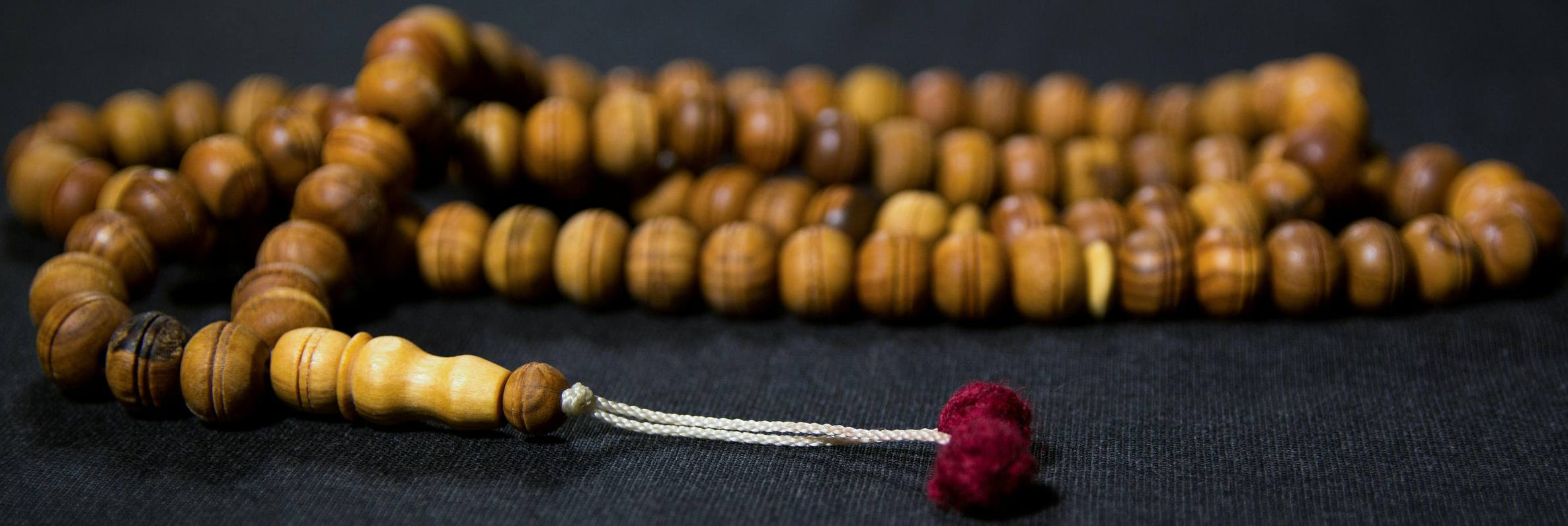 Wooden prayer beads with a red tassel on a dark background